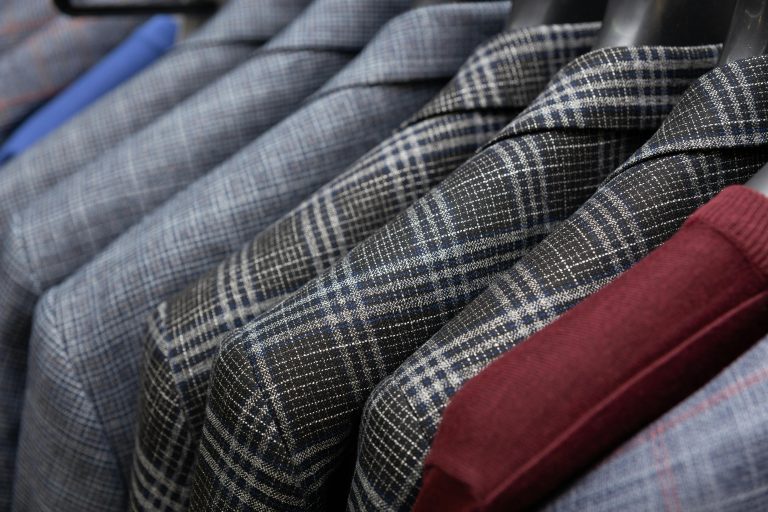 A detailed view of classic men's suits in different patterns hanging in a wardrobe.